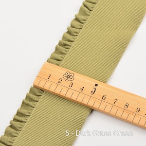 May include: A close-up of a green ruffled trim fabric with a wooden ruler marked with numbers 1 through 9. The text "5 - Dark Grass Green" is visible below the ruler.