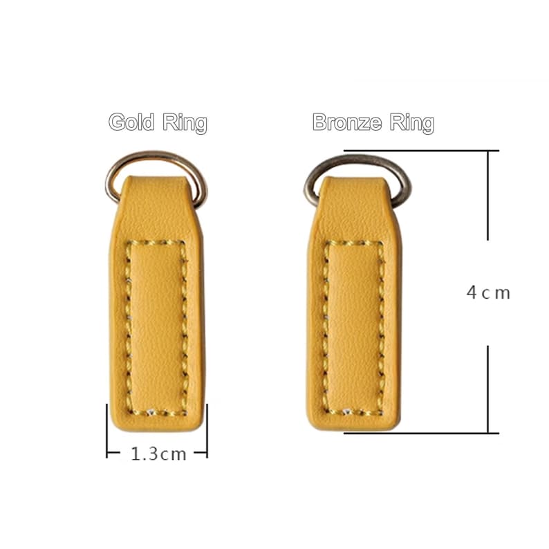 Op de afbeelding: Twee gele leren sleutelhangers met metalen ringen. E&eacute;n heeft een gouden ring, de andere een bronzen ring. Elke sleutelhanger is 1,3 cm breed en 4 cm lang. De tekst "Gold Ring" en "Bronze Ring" staat erboven.