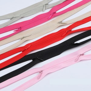 Könnte beinhalten: Sortiment an Reißverschlussbändern in verschiedenen Farben, darunter Schwarz, Rot, Rosa, Beige und Grau. Die Reißverschlüsse sind doppelseitig und haben eine glatte Oberfläche.