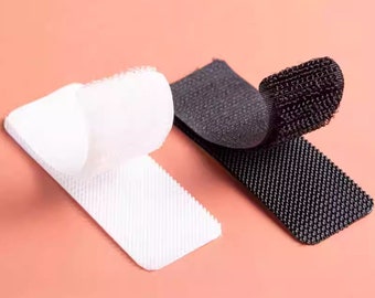 May include: A close-up of two pieces of hook and loop fastener tape. One piece is white and the other is black. Both pieces are folded in half, showing the hook side of the tape.