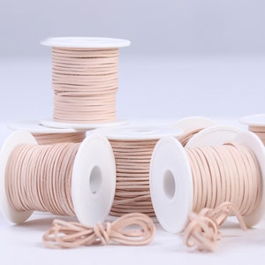 May include: Spools of light beige leather cord wound around white spools. The cord is approximately 1/8 inch thick.