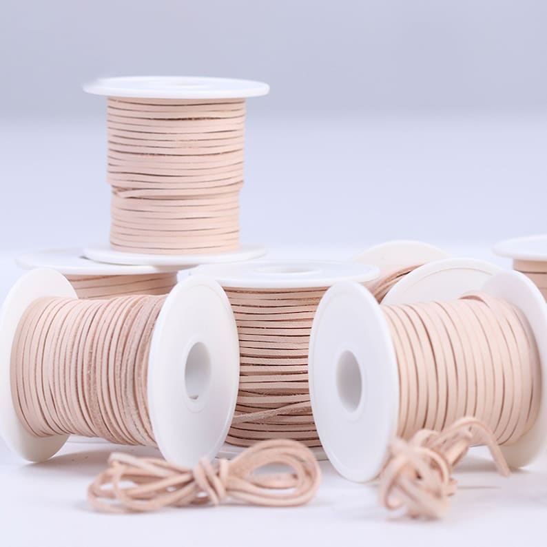 May include: Spools of light beige leather cord wound around white spools. The cord is approximately 1/8 inch thick.