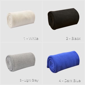 May include: Four rolls of knit fabric in different colors: white, black, light gray, and dark blue. The fabric is rolled up and the ends are visible. The fabric is a ribbed knit.