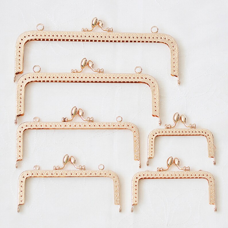 May include: Set of five gold-toned metal purse frames with decorative details. The frames are different sizes and are arranged in a row from largest to smallest.