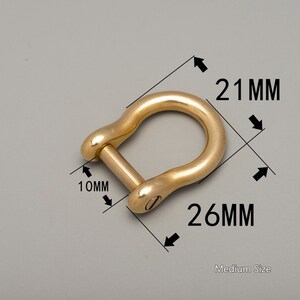 May include: A medium-sized, gold-colored shackle with a pin closure. The shackle measures 26 mm long, 21 mm wide, and 10 mm thick. The text "Medium Size" is visible. The shackle is on a gray background.