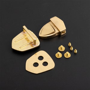 May include: A set of gold-toned metal hardware for leather goods, including a buckle, a plate with three holes, and six screws.