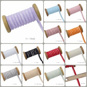 May include: Twelve spools of ruffled trim in various colors, including sky blue, pink, dark pink, orange, white, black, red, light yellow, gray, beige, light green, and violet. Each spool is wrapped in wood and has a label with a number and color name.