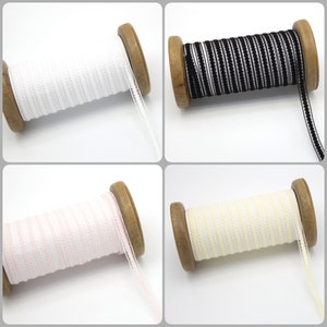 May include: Four spools of elastic trim with different colors. The trim is white, black, pink, and yellow. Each spool is made of wood and has a white background.