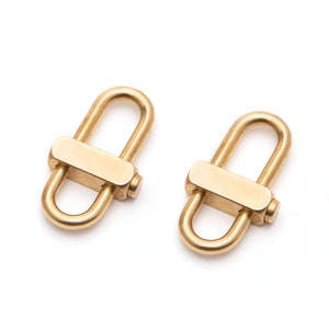 May include: Two gold-toned metal clasps, each with a D-shaped ring and a rectangular bar across the opening. The clasps are designed to be used as connectors for jewelry or other crafts.