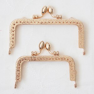 May include: Two gold-toned metal purse frames with ornate designs. The frames are open and ready to be used for a DIY purse project.