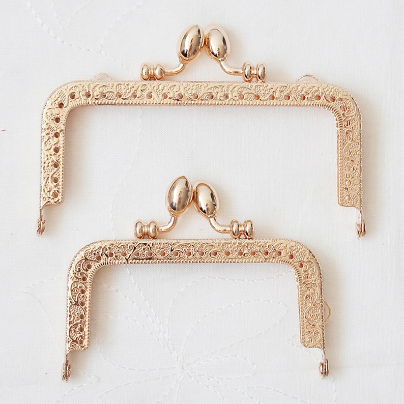 May include: Two gold-toned metal purse frames with ornate designs. The frames are open and ready to be used for a DIY purse project.