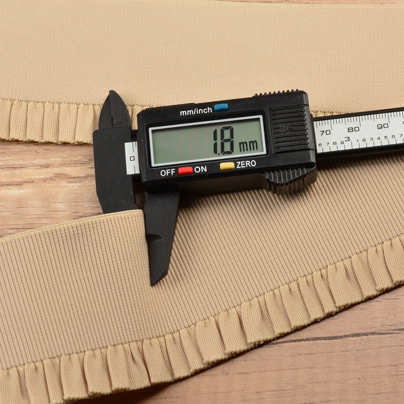 May include: A close-up of a beige elastic trim with a ruffled edge. A digital caliper measures the trim at 18 mm.