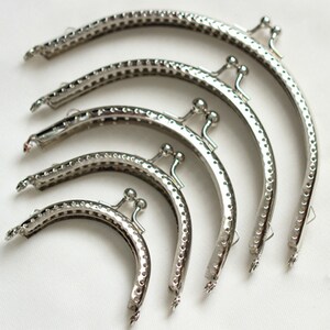 May include: Five silver-toned purse frames of different sizes. The frames are made of metal and have a decorative pattern. They are used for making purses and wallets.