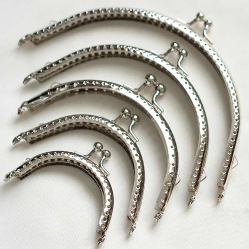 May include: Five silver-toned purse frames of different sizes. The frames are made of metal and have a decorative pattern. They are used for making purses and wallets.