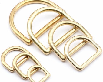 May include: Set of four gold-toned metal D-rings of varying sizes. The rings are smooth and polished.