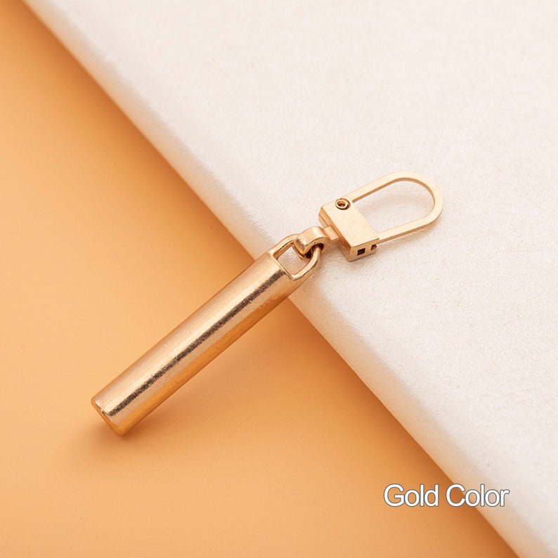 May include: Gold-colored earring with a long, cylindrical bar and a hook closure.