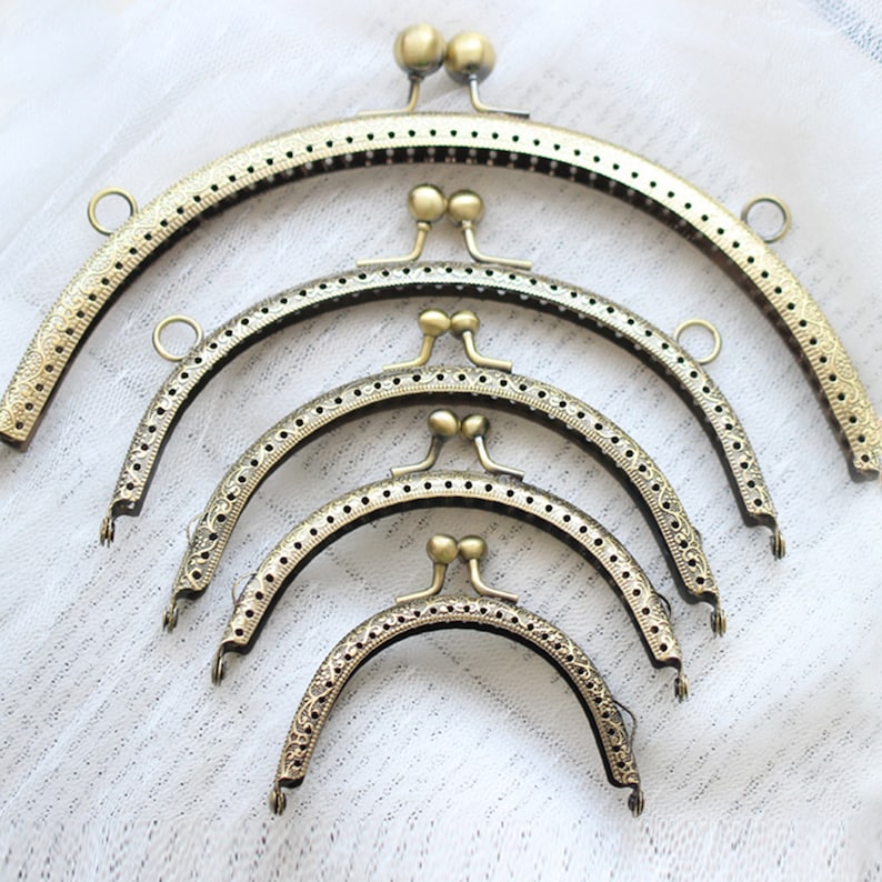 May include: Five antique gold-toned metal purse frames of varying sizes. The frames are all half-circle shaped and have a decorative pattern around the edge.