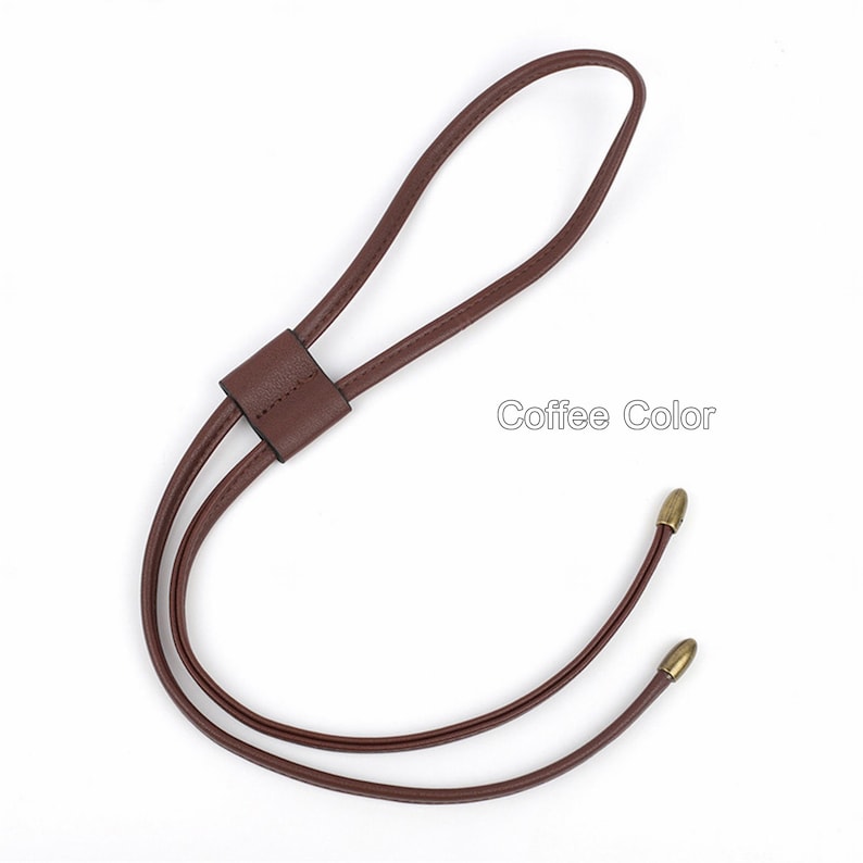May include: A brown leather cord with gold-toned metal tips. The cord has a loop at the top and two strands that come together at the bottom. "Coffee Color" is written in white text on a white background.