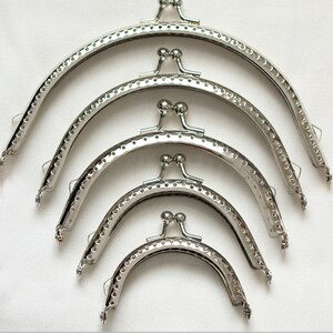 May include: Four silver-toned purse frames of different sizes. The frames are made of metal and have a rounded shape. They are designed to be used for making purses or wallets.