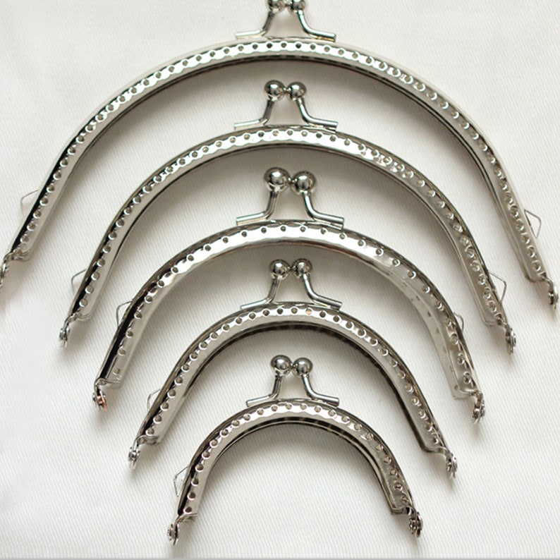 May include: Four silver-toned purse frames of different sizes. The frames are made of metal and have a rounded shape. They are designed to be used for making purses or wallets.