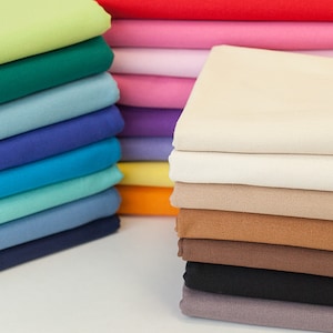May include: A stack of fabric swatches in various colours, including green, blue, orange, and brown. The swatches are folded neatly and arranged in a vertical stack.