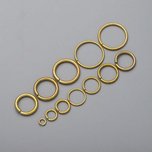 Könnte beinhalten: Ein Satz mit 10 goldenen Sprungringen in verschiedenen Größen. Die Ringe sind diagonal von der größten zur kleinsten Größe angeordnet.