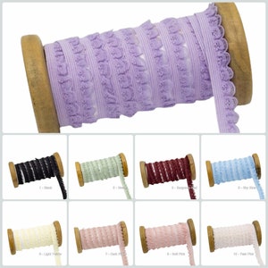 Op de afbeelding: Tien spoelen elastische trim met een gegolfde rand en een decoratief patroon. De trim is verkrijgbaar in verschillende kleuren, waaronder zwart, groen, bordeauxrood, hemelsblauw, lichtgeel, donkerroze, roze en lichtroze.