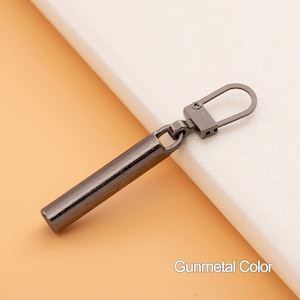 May include: Gunmetal colored zipper pull with a long, cylindrical slider and a loop at the top.