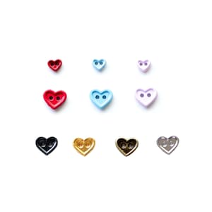 Puede incluir: Surtido de botones en forma de corazón en varios colores, incluyendo rojo, azul, morado, negro, dorado y plateado. Los botones tienen dos agujeros cada uno.