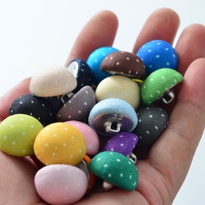 Puede incluir: Una colección de botones de tela coloridos con lunares blancos. Los botones son de varios colores, incluyendo verde, azul, amarillo, rosa, morado y marrón. Los botones son todos del mismo tamaño y forma, y están dispuestos en una pila.