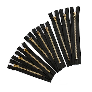 May include: A collection of black zipper closures with gold metal pulls. The zippers are arranged in a fan shape.