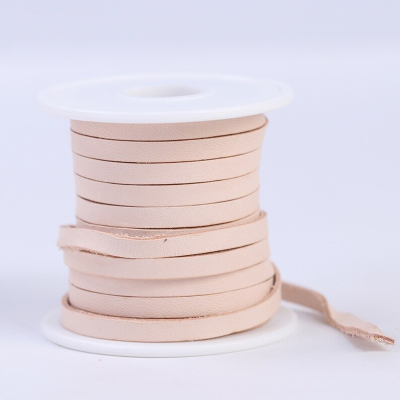 May include: A spool of light pink leather cord, wound around a white plastic spool. The cord is about 1/4 inch wide.