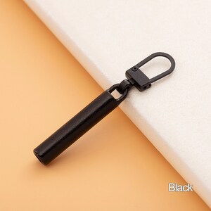 May include: Black metal zipper pull with a long, cylindrical shape and a loop at the top.
