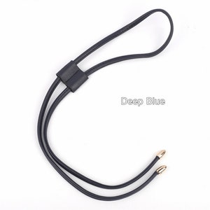 May include: A dark blue leather strap with gold-toned metal tips. The strap has a loop at the top and is designed to be used as a necklace or a bag strap.