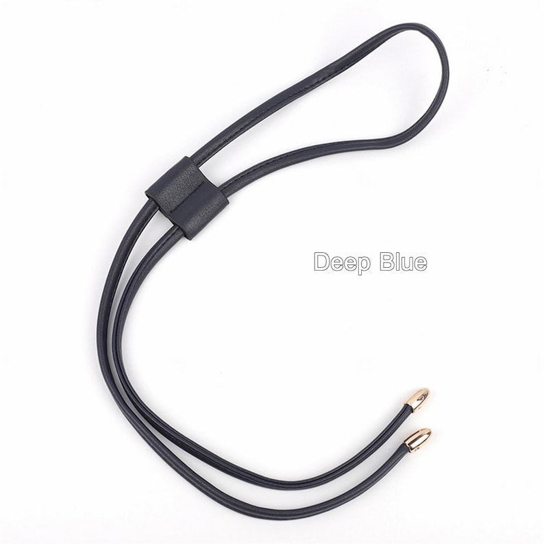 May include: A dark blue leather strap with gold-toned metal tips. The strap has a loop at the top and is designed to be used as a necklace or a bag strap.