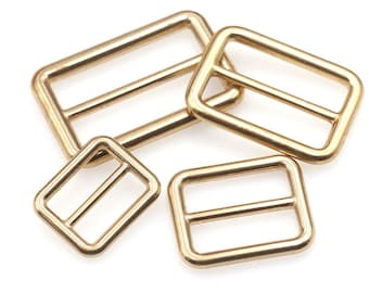 May include: Four gold-toned metal slider buckles of different sizes. The buckles are rectangular with a center bar.