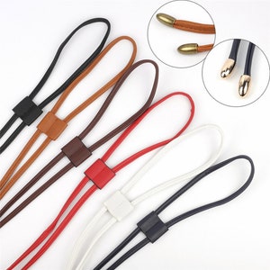 May include: Five different colored leather cords with gold metal tips. The cords are tied together in a knot at the top and have a square loop at the bottom. The cords are brown, black, red, white, and blue.