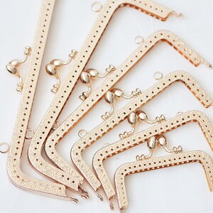 May include: A set of six gold-toned metal purse frames with intricate floral designs. The frames are of varying sizes and are arranged in a staggered pattern.