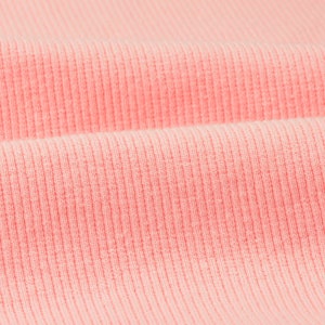 May include: Close-up of a soft, pink ribbed fabric. The fabric has a subtle texture and a smooth, even surface.