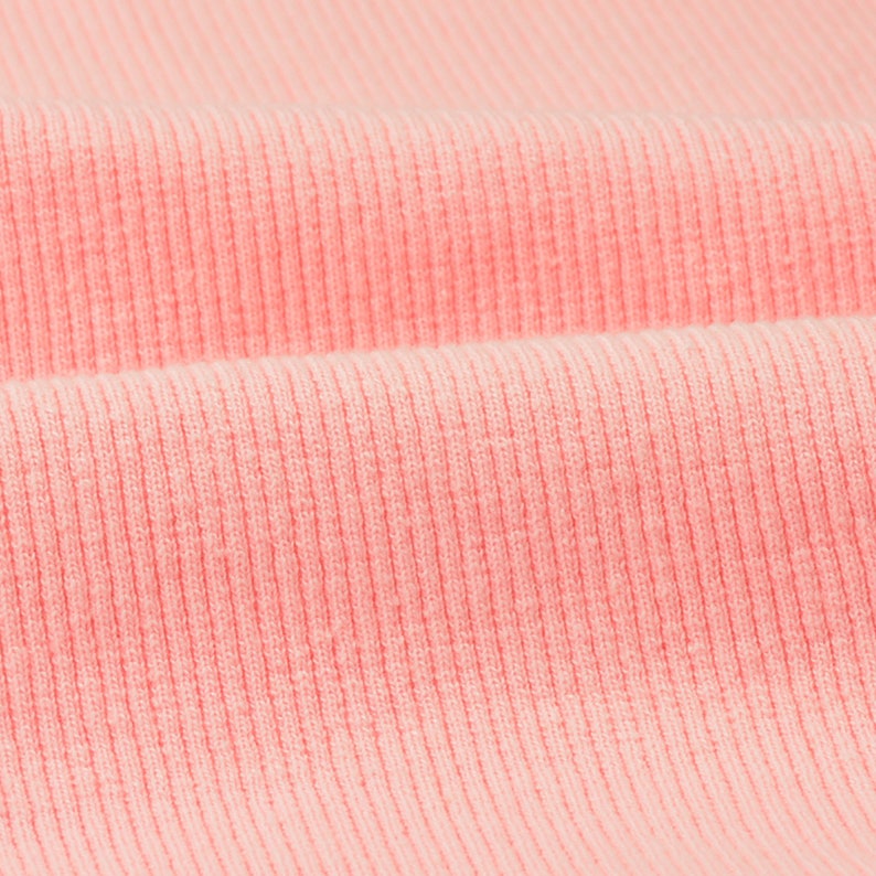 May include: Close-up of a soft, pink ribbed fabric. The fabric has a subtle texture and a smooth, even surface.
