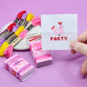 May include: A cross-stitch project with a pink chicken design and the word "PARTY" in red. The image shows pink and yellow embroidery threads, and two pink matchbox kits labelled "HEN PARTY". The kits feature a cartoon chicken wearing a hat.