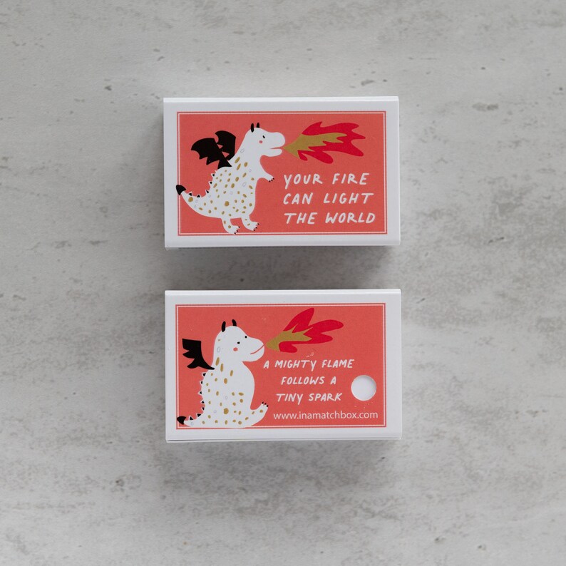 May include: Two white matchboxes with red backgrounds and a white dragon illustration. The top matchbox says "Your fire can light the world". The bottom matchbox says "A mighty flame follows a tiny spark" and "www.inamatchbox.com".