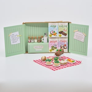 May include: A miniature kitchen scene featuring a light green cabinet with baking mix boxes labelled Icing, Yule Log, Wreath, and Cookie. Includes tiny glass jars, a baking drawer, and a red chequered cloth with miniature baked goods.