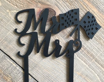 Könnte beinhalten: Schwarzer Acryl-Kuchentopper mit den Worten "Mr & Mrs" in einer kursiven Schrift. Zwei schwarze karierte Flaggen sind am Topper befestigt.