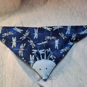 Könnte beinhalten: Ein dreieckiges Haustier-Bandana mit einem marineblauen Stoff mit Libellenmuster. Ein hellblaues Mäusegesicht mit Ohren, Augen und Schnurrhaaren ist auf das Bandana genäht. Das Bandana ist für Haustiere konzipiert.