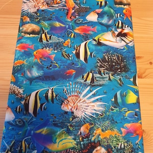 Könnte beinhalten: Ein farbenfroher Stoff mit blauem Hintergrund, der eine Vielzahl von tropischen Fischen, Seepferdchen und Korallenriffen zeigt. Der Stoff ist perfekt für Bastelarbeiten, Wohnaccessoires oder Kleidung.