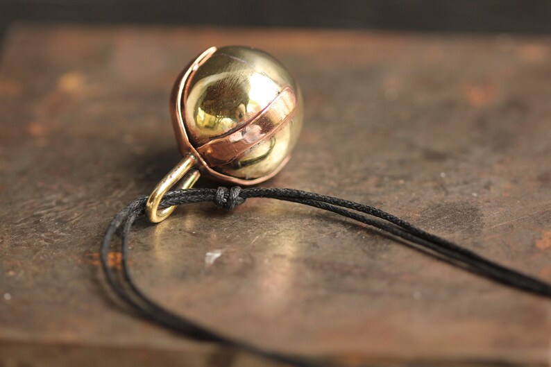Brass Ball Pendant with a Copper X across the top on a Black Leather cord.