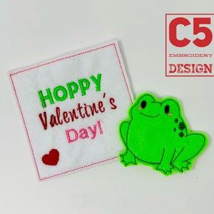 May include: A green felt frog with black spots and a red heart on a white felt background with the text "Hoppy Valentine's Day!" in green and pink embroidery.