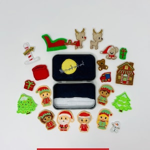 May include: A set of felt Christmas ornaments in a tin box. The ornaments include Santa Claus, elves, reindeer, a snowman, a Christmas tree, a house, a gift, and a sleigh. The tin box has a moon and stars on the lid. The text "C5 DESIGNS" is printed on the bottom of the image.