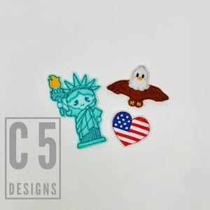 May include: Three embroidered patches featuring American patriotic symbols: a blue and green Statue of Liberty, a brown bald eagle with white head and a red, white and blue heart with stars.